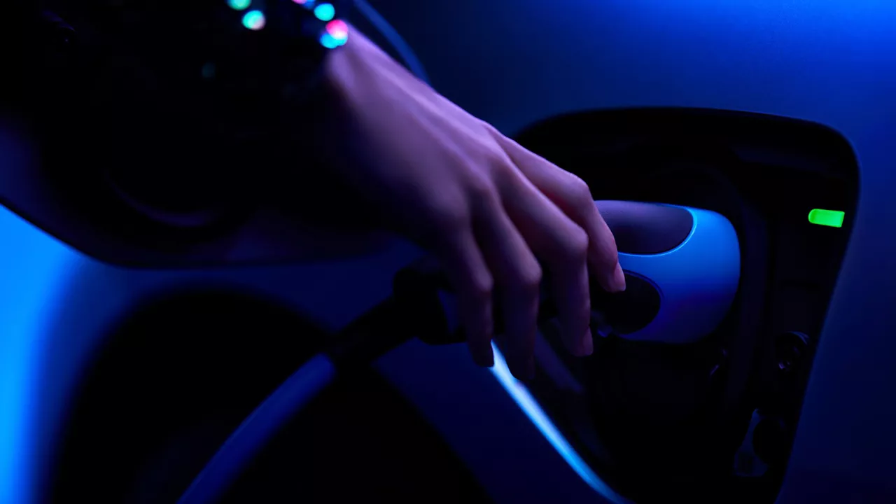 Ruka zapojuje nabíječku do hybridního auta v režimu EV.