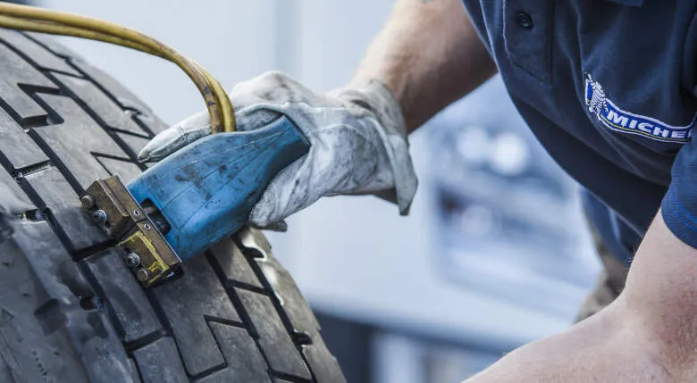 Mechanik měří tloušťku pneumatiky nákladního vozidla pomocí speciálního nástroje.