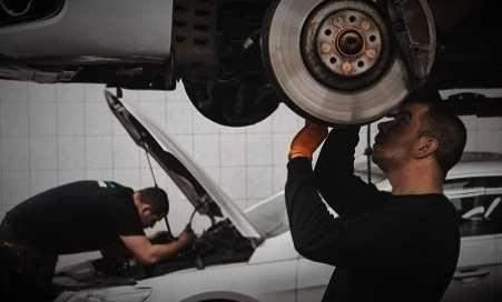 Mechanici opravují auto s otevřenou kapotou v dílně.