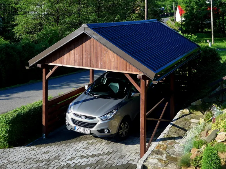 Stříbrné auto pod přenosnou garáží s dřevěným rámem.