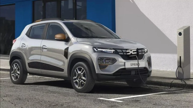 Stříbrné elektromobilové auto nabíjené u zdi.