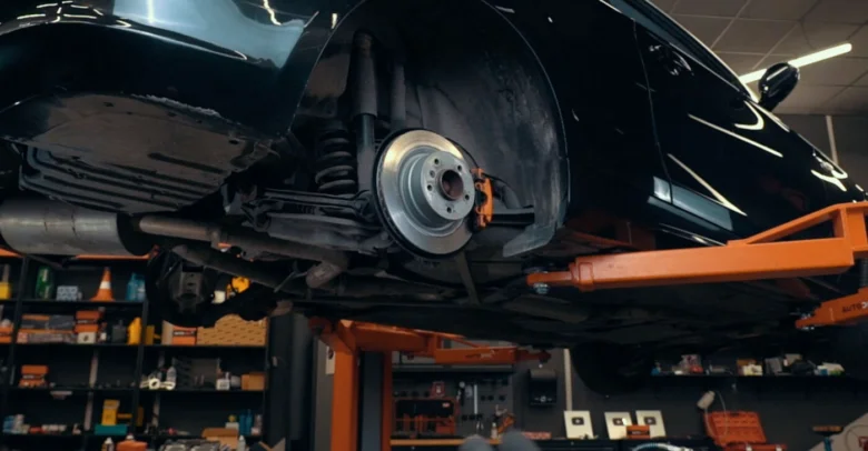 Černé auto na zvedáku v dílně s viditelnou brzdovou soustavou.