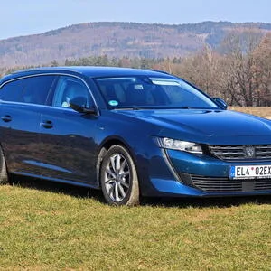 Modrý vůz s elektromotorem zaparkovaný na trávě před kopci.