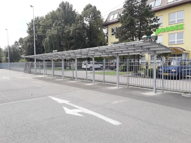 Parkoviště vedle plotu s přístřeškem pro kola u budovy.