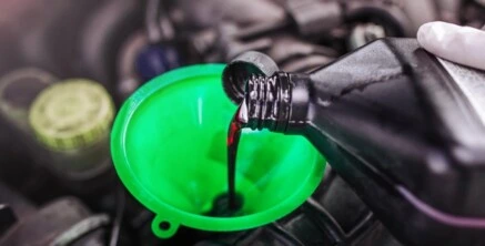 Nalévání oleje do motora auta zeleným lejnkem.