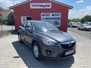 Šedý SUV Mazda CX-5 zaparkovaný před červenou budovou.