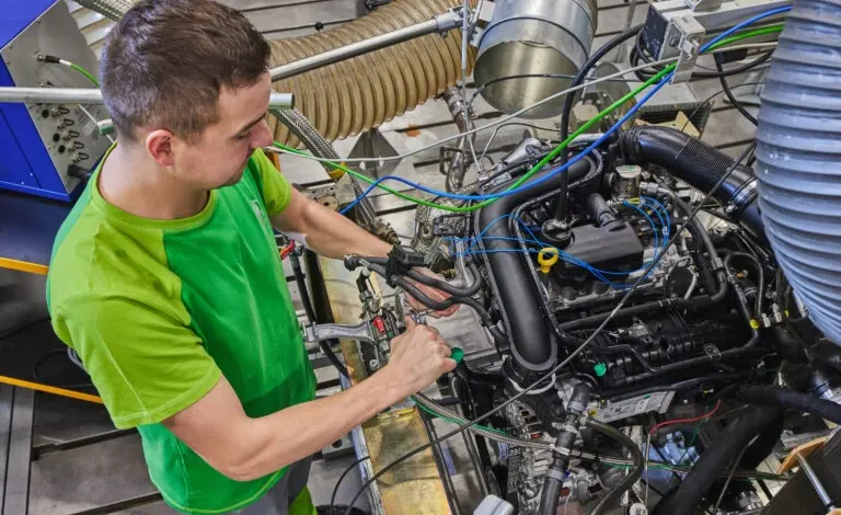 Technik montuje motor v továrně s hadicemi a nástroji.