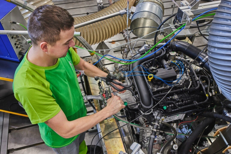 Technik montuje motor v továrně s hadicemi a nástroji.