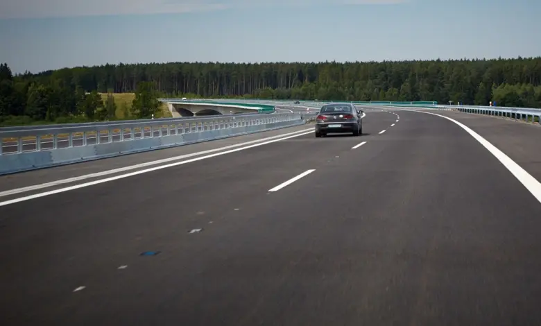 Automobil jede po dálnici přes most v lesnatém prostředí.