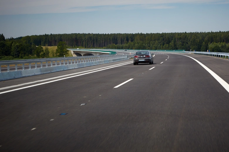 Automobil jede po dálnici přes most v lesnatém prostředí.