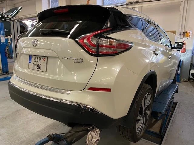 Bílý automobil na zvedáku v autoservisu při výměně nárazníku.