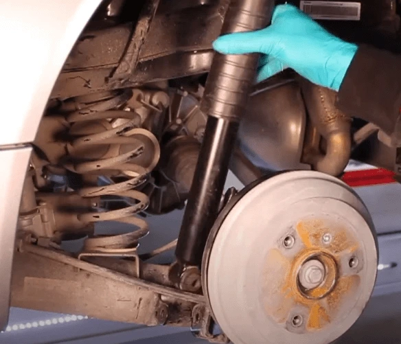 Mechanik kontroluje opotřebení tlumiče u kola s viditelným brzdovým kotoučem.