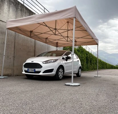 Bílý automobil pod přenosnou garáží pro ochranu před sluncem.
