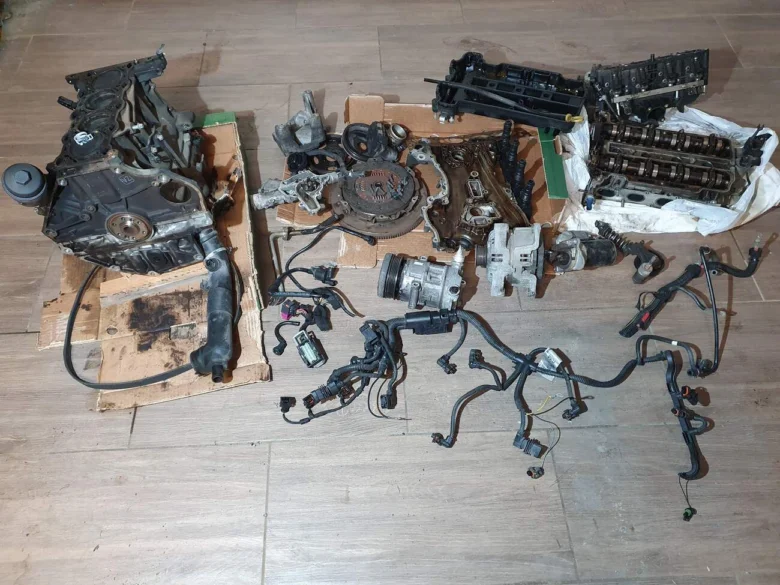 Rozložené díly motoru pro výměnu u automobilu na podlaze.