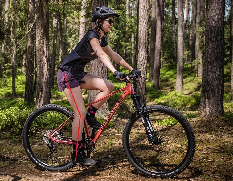 Žena na horském kole v lese ukazuje správnou polohu pro dospělé cyklisty.