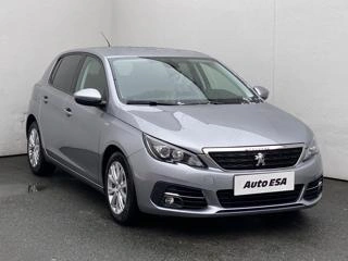 Stříbrný hatchback Peugeot 308 zaparkovaný před bílou zdí.