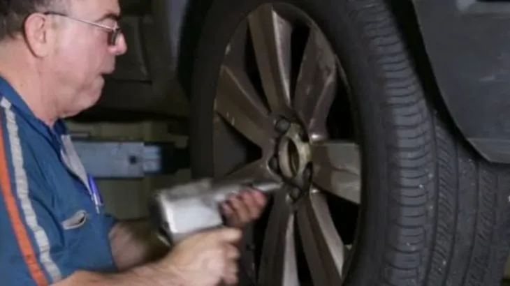 Mechanik utahuje šrouby kola pomocí nářadí.