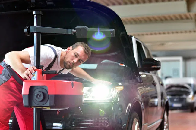 Mechanik nastavuje světlomety auta pomocí diagnostického zařízení.