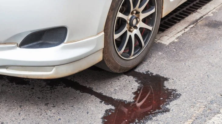 Bílé auto s únikem kapaliny na asfaltovou silnici.