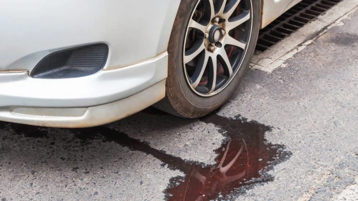 Červená brzdová kapalina unikající pod kolo auta na asfaltu.