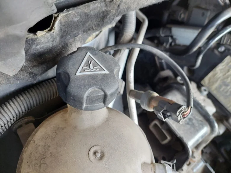 Nálevka pro chladicí kapalinu s varovným štítkem v motorovém prostoru.