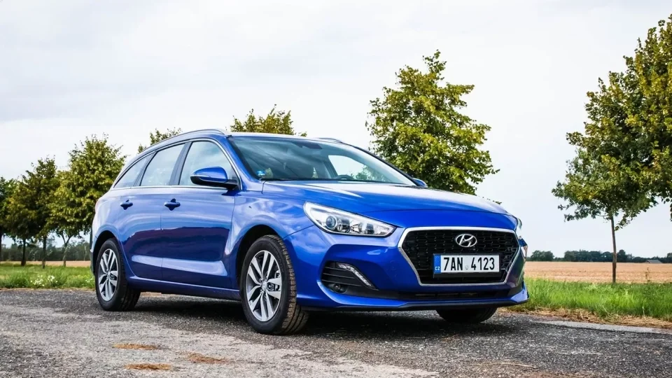 Modrý vůz Hyundai i30 na venkovské cestě mezi stromy.