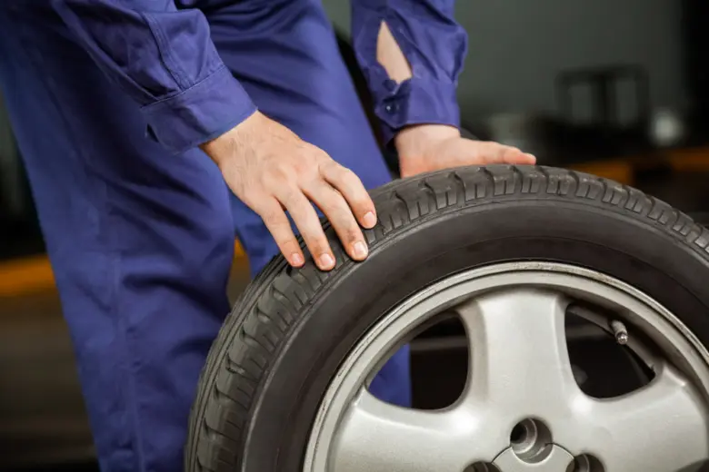Mechanik v modrém obleku drží pneumatiku s nárazníkem.