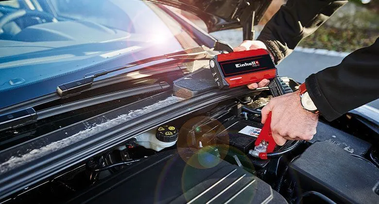 Muž připojuje červený externí startér k autobaterii pod kapotou.