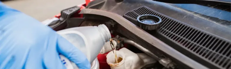 Ruka v rukavici nalévá chladicí kapalinu do rozšiřovací nádrže.