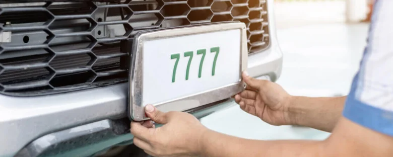 Osoba připevňuje registrační značku na předek automobilu.