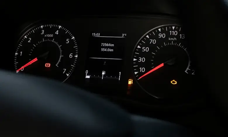 Přístrojová deska s rozsvícenou kontrolkou motoru a nízkým palivem.