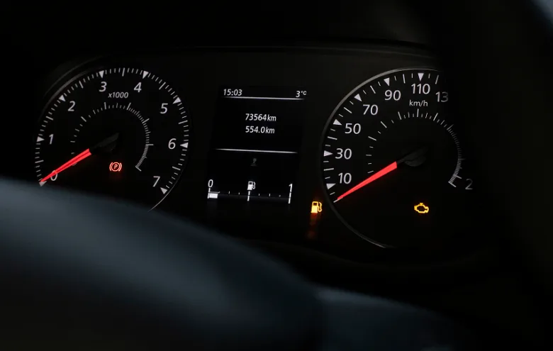 Přístrojová deska s rozsvícenou kontrolkou motoru a nízkým palivem.