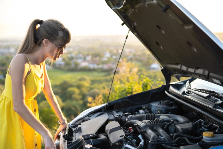 Žena kontroluje motor auta s otevřenou kapotou venku.