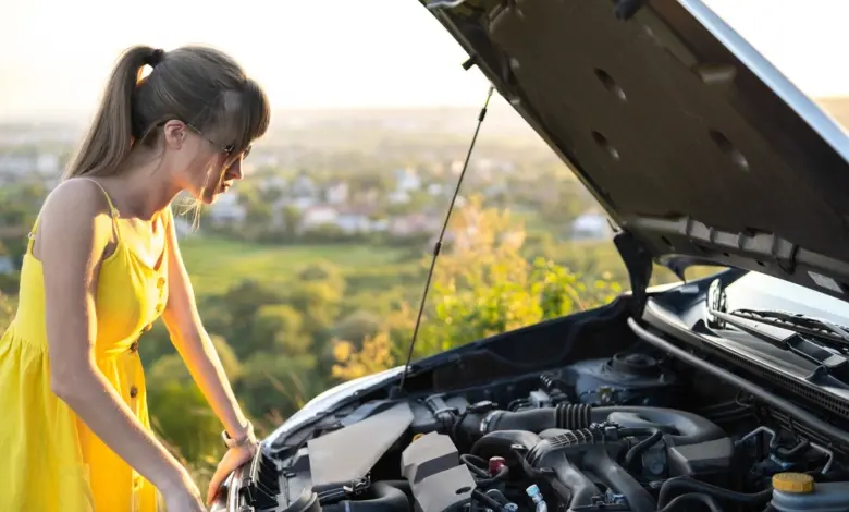 Žena v žlutém šatě kontroluje motor vozu s otevřenou kapotou.