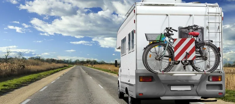 Bílý rekreační vůz s bicykly na zadním nosiči přesahující rozměry.