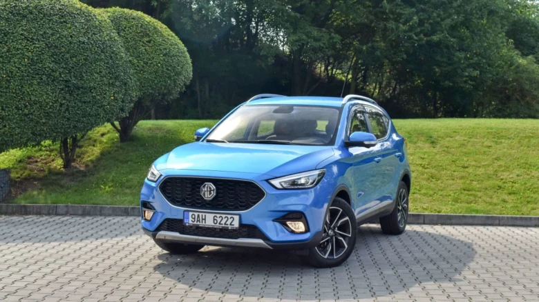 Modrý automobil MG zaparkovaný na dlažbě před zelenou trávou.