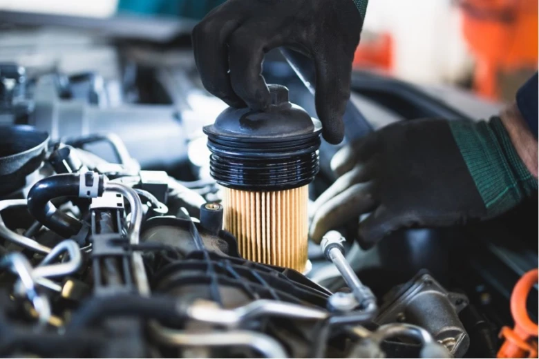 Mechanik instaluje nový palivový filtr do motoru automobilu.