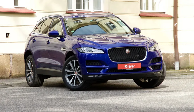 Modrý SUV Jaguar F-Pace zaparkovaný před budovou.