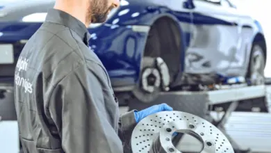 Mechanik drží brzdový kotouč u modrého auta v dílně.