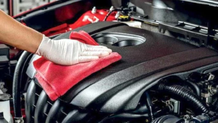 Ruka v rukavici čistí kryt motoru červenou utěrkou.