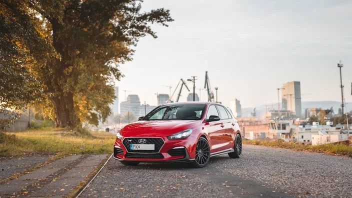Červený vůz Hyundai zaparkovaný na silnici s městem v pozadí.