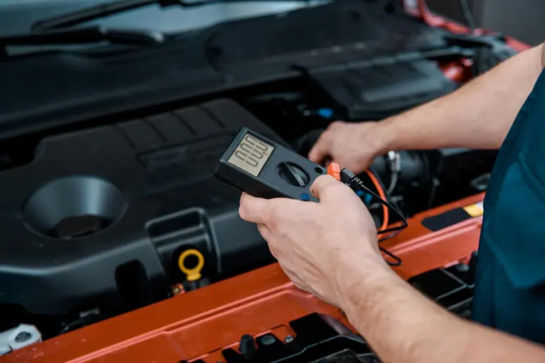 Mechanik měří stav autobaterie multimetrem pod kapotou.