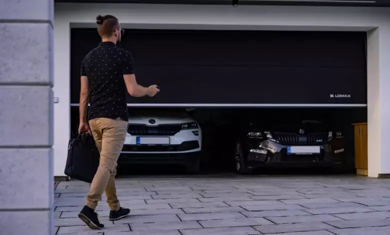 Muž otevírá dvoudveřovou garáž s dvěma auty uvnitř.