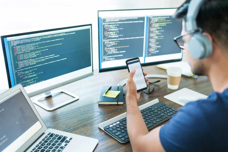 Muž pracuje na kódu u počítače s více monitory.