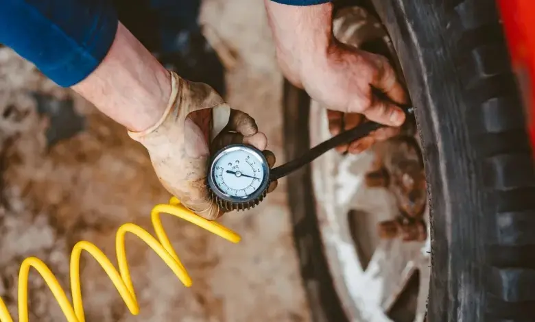 Mechanik měří tlak vzduchu v pneumatice pomocí manometru.