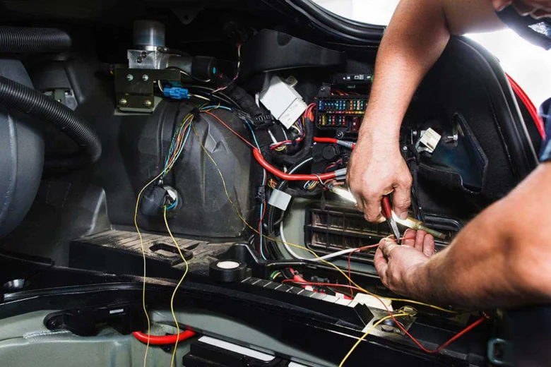 Mechanik opravuje elektrické součásti pod kapotou automobilu.
