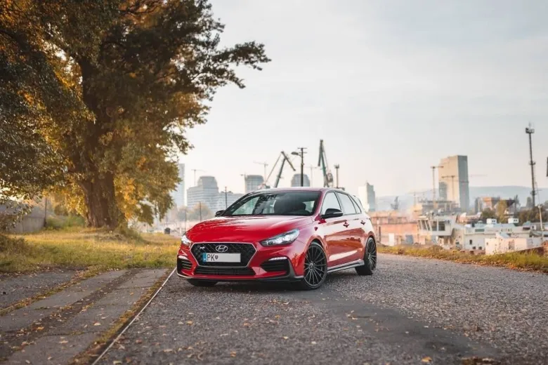 Červený hatchback Hyundai i30 na zemi s městem v pozadí.