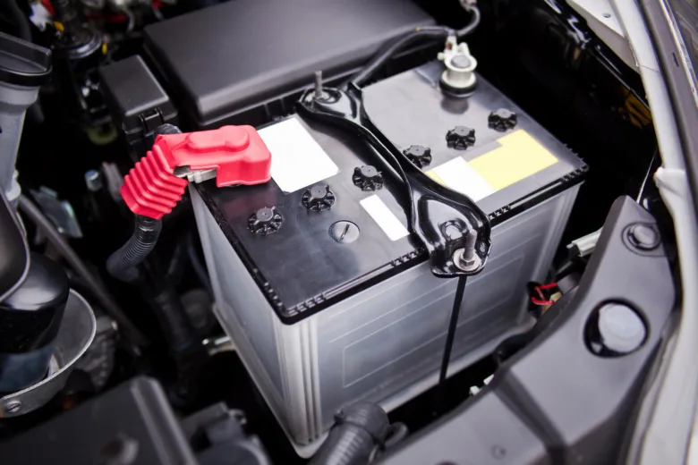 Autobaterie s červeným krytem na kladném pólu pod kapotou.
