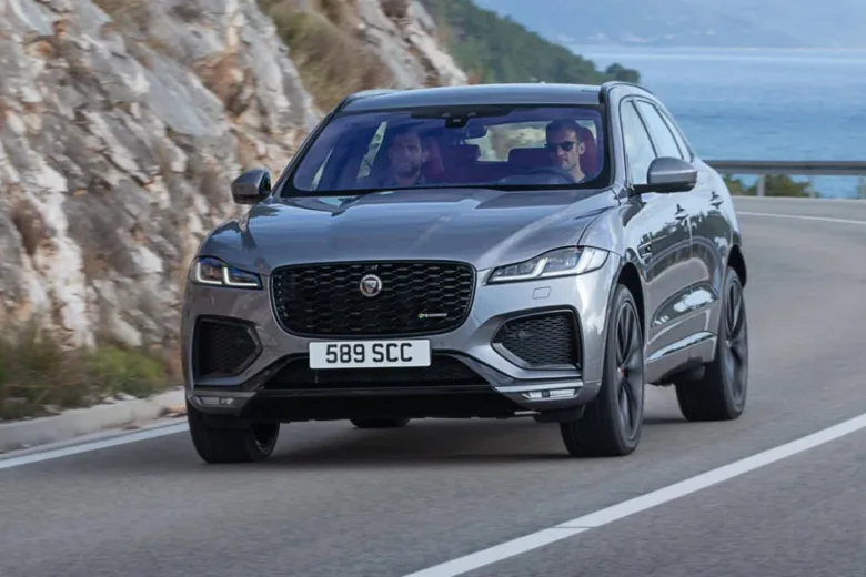 Stříbrný Jaguar F-Pace jede po pobřežní silnici s mořem v pozadí.