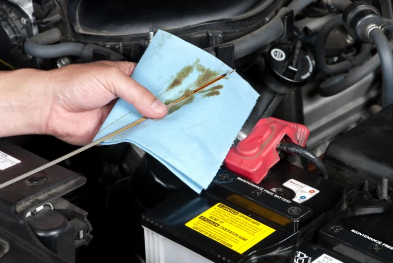 Ruka čistí olejovou tyčinu v motoru automobilu papírovou utěrkou.